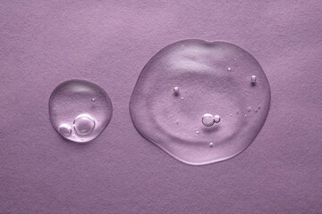 A drops of transparent cosmetic gel on a purple background.