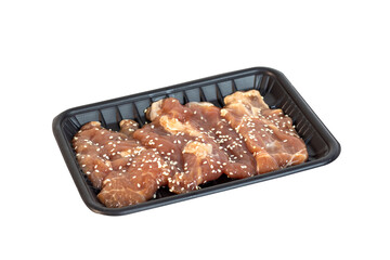 Side view of raw pork slices marinated in white sesame seeds on a black plastic tray. Isolated on a white background buffet menu. Meat prepared for yakiniku or sukiyaki
