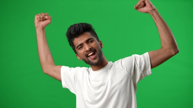 Excited handsome Middle Eastern football player gesturing victory posing on green screen. Portrait of satisfied successful young sportsman looking at camera smiling at chromakey background