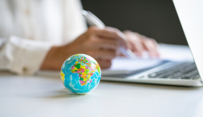 Close up view of world globe with businesswoman and computer laptop at the background. Copy space. - obrazy, fototapety, plakaty