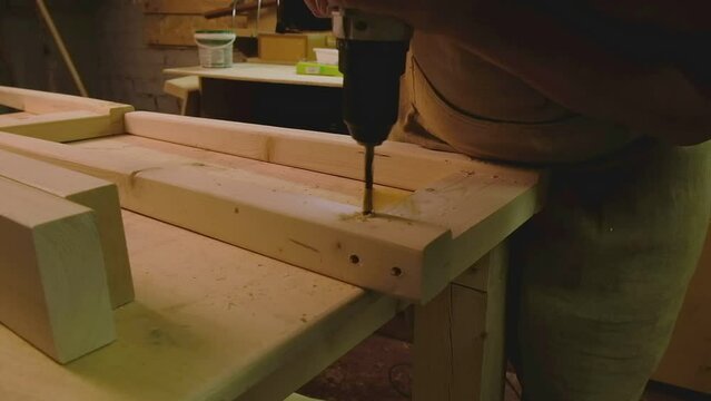 The master makes holes with a drill in wood parts