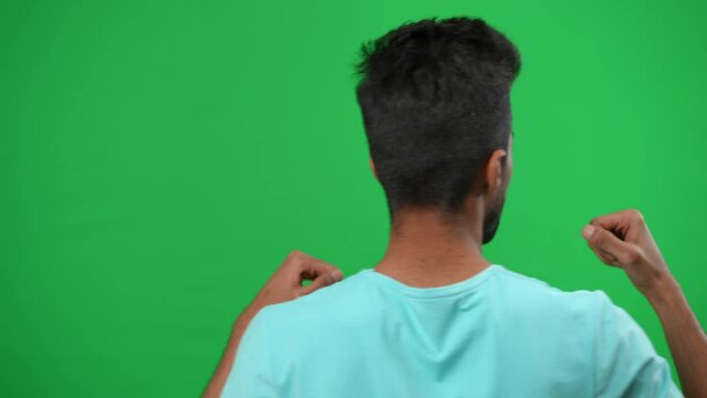Back view motivated Middle Eastern man gesturing cheering for football team on green screen. Young excited sport fan supporting game on championship at chromakey background mockup