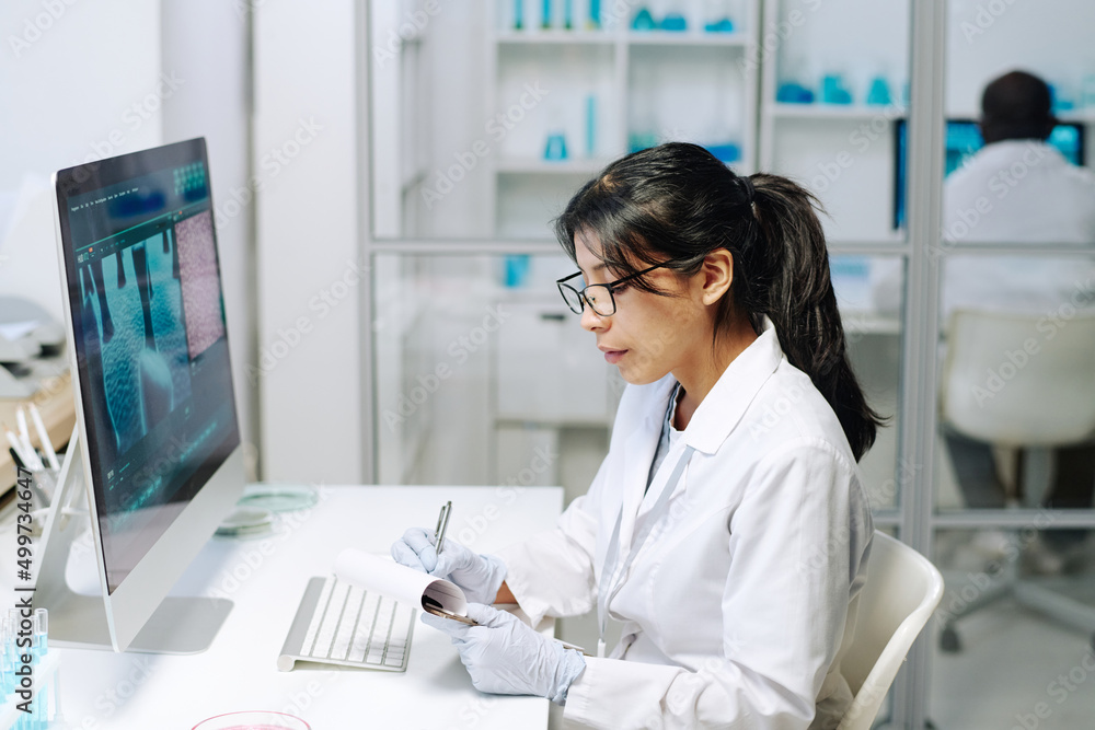 Poster contemporary young female researcher in whitecoat and gloves making scientific notes in notepad whil