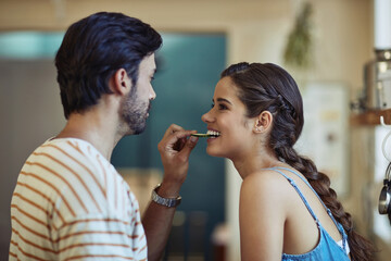 Love makes everything taste better. Shot of an affectionate young couple snacking while preparing a meal in their kitchen.