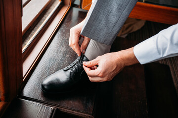 Groom tying shoelaces on black stylish shoes on a wooden brown floor indoors in the morning