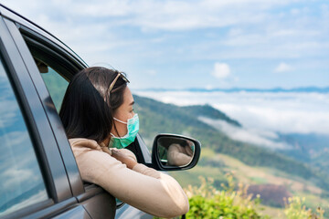 Pretty young woman sitting in a car watching a beautiful mountain view. Asian Girl in surgical mask having fun at the trip. Driving road trip on vacation and adventure concept