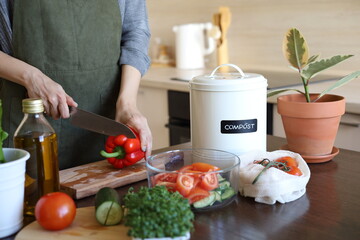 Young asian vegan woman cutting vegetables in the kitchen. Compost bucket. Eco friendly person.