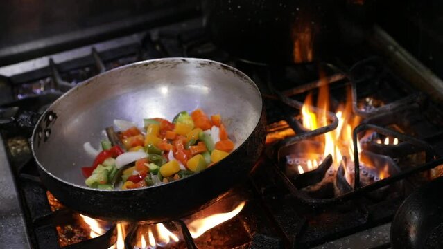 Asian cuisine. Closeup view of the chef cooking sliced vegetables in the wok pan. The chef shakes the wok. 