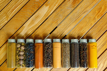 Different multi-colored indian spices in transparent jars lie on a wooden background with copy space
