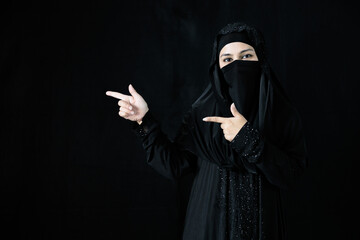 muslim woman in hijab and pointing pose on black background