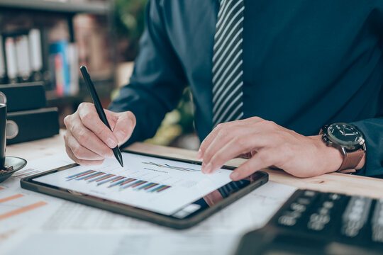 Business hand hold stylus pen touch screen digital tablet with business diagram on the table workspace.