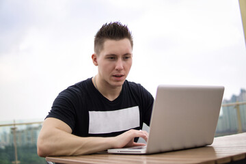 Young professional businessman wearing casual clothes and using modern laptop outdoors in a cafeteria.