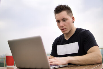 Young professional businessman wearing casual clothes and using modern laptop outdoors in a cafeteria.