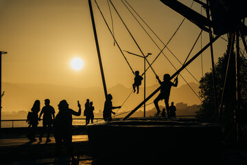 children jumping in trampoline high into the sunset sky safed with elastic safety belt