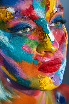 Stay colourful. Studio shot of a young woman posing with multi-coloured paint on her face.