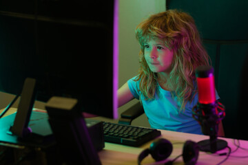 Child playing computer games or studying on pc computer. Kid gamer on night neon lighting. Distance education concept. Kids online working, gaming on a desktop computer pc.