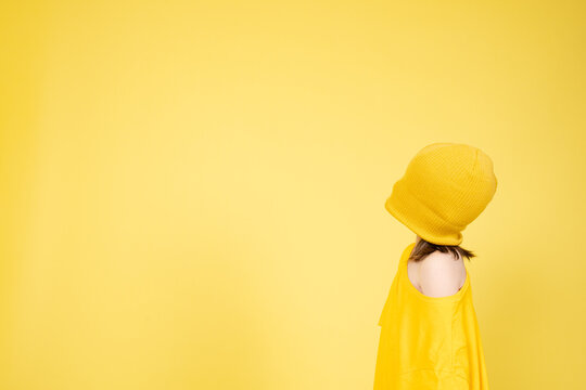 Child covering eyes with wool hat isolated on yellow background. Blindfolded little girl looking at copy space. Anxiety, fear and depression concept.