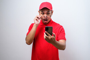Asian delivery man wearing red shirt looks surprised at the good news he received from his smartphone.