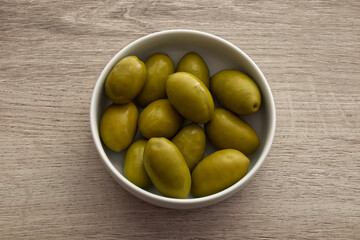 Bowl of giant green olives with a stone isolated on wooden background