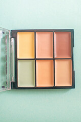 Make-up palette with colorful concealers on mint background.