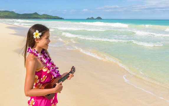 Hawaii luau ukulele hula dancing woman playing ukulele guitar on beach vacation travel wearing flower lei necklace and paero. Multiracial Asian dancer smiling on hawaiian travel vacation