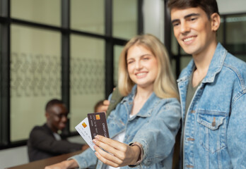 Cheerful young couple check in at hotel reception counter, female holding two credit card.