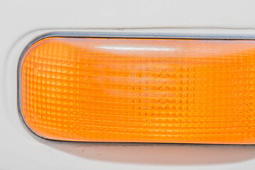 Closeup of orange turn signal reflector on side of white vehicle.