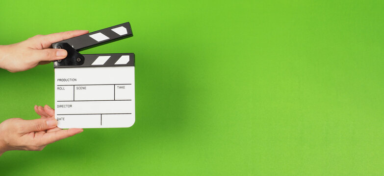 The hands are holding a small clapper board or movie slate on the green screen background.