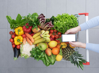 Woman buying fresh greens and using her smartphone