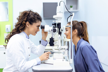 Eye doctor with female patient during an examination in modern clinic. Ophthalmologist is using special medical equipment for eye health saving and improving. - Powered by Adobe