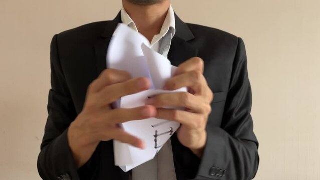 Frustrated asian male businessman professional crumpling paper with written message &ldquo;VIRTUE SIGNALLING&rdquo; word. Man in suit and tie having nervous breakdown furiously throwing crumpled paper at work