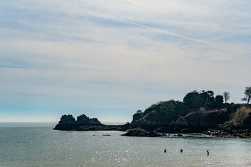 A sunny backlit headland and inlet where three people are swimming