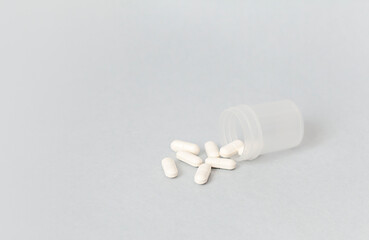 white pills spill out of a plastic container on a gray background