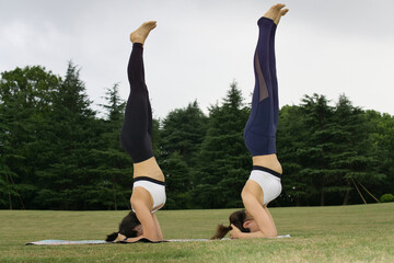Two young Asian women practicing yoga outdoors. 