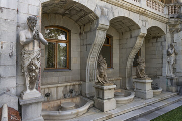 Fototapeta premium Ancient statues near the walls of the historical Massandra Palace (Yalta, Crimea) in summer. close-up of the details of the facade. Stone satyrs and chimeras, water bowls as exterior decoration