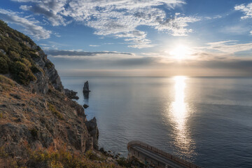 Sunny seascape with high cliffs, blue sky with floating white clouds and reflection of sunshine in the water in the form of a path. Morning view from the cliff to the fabulous sunrise in the Crimea