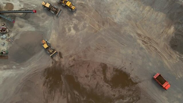 Loaders, tractors and a dump truck drive off the gravel pile at the river port. View from above.