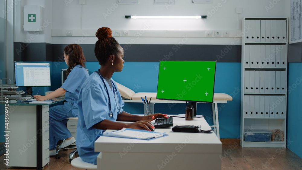 Poster medical assistant using computer with horizontal green screen in doctors office. woman working as nu