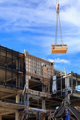 An office building being demolished. A crane is lowering workers on a work platform