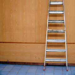 A folded aluminum stepladder stands against the wall