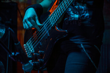 The bass guitarist plays the bass guitar. Dark key. Selective focus - obrazy, fototapety, plakaty