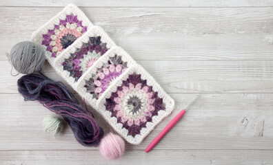 Granny squares crochet in pink and purple shades , a hook and yarn balls.