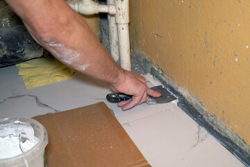 A worker puts a spatula on the floor when laying ceramic floor tiles. Selective focus