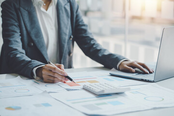 Business woman using a calculator to check income and budget and analyzing graphs in office.