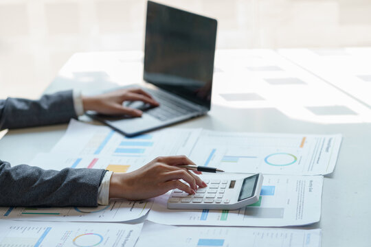 Business woman using a calculator to check income and budget and analyzing graphs in office.