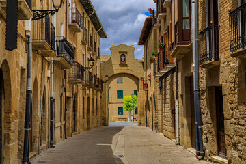 Fototapeta na wymiar Rustic medieval stone houses on a street with an archway leading to a plaza in Olite, Spain famous for a magnificent Royal Palace castle