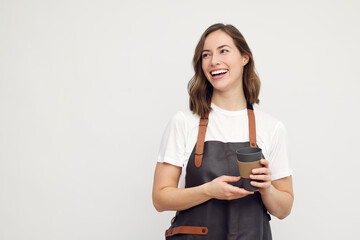Portrait of beautiful young barista woman looking left and smiling or laughing, while holding a to-go coffee in hand. Isolated on white background.