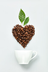 White coffee cup and coffee beans in shape of heart on white background, flat lay