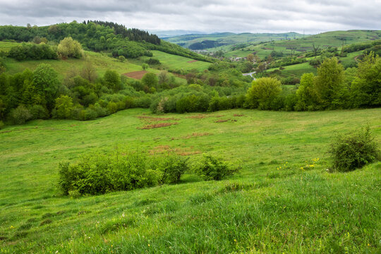 carpathian countryside landscape in spring. grassy meadows, rural fields and forested slopes on hills rolling off in to the distant village in the valley. overcast rainy weather with above the ridge