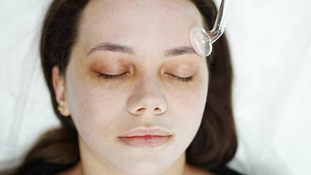 Beautician uses the darsonval device on the client's face. Professional skin care in the salon. The concept of cosmetology and rejuvenation.